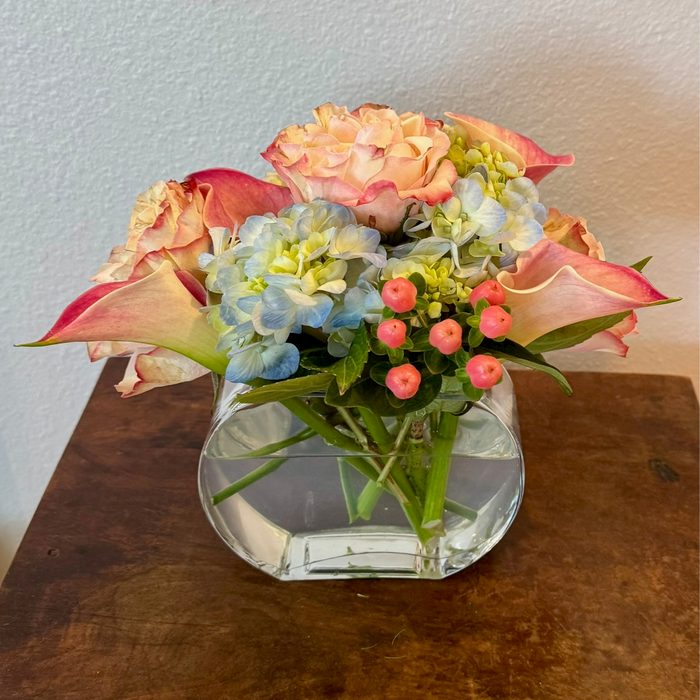Peach rose, blue hydrangea, and pink hypericum berries in a glass vase