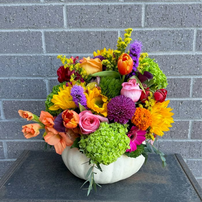 Vibrant fall arrangement with sunflowers, pink roses, and mums in a white pumpkin