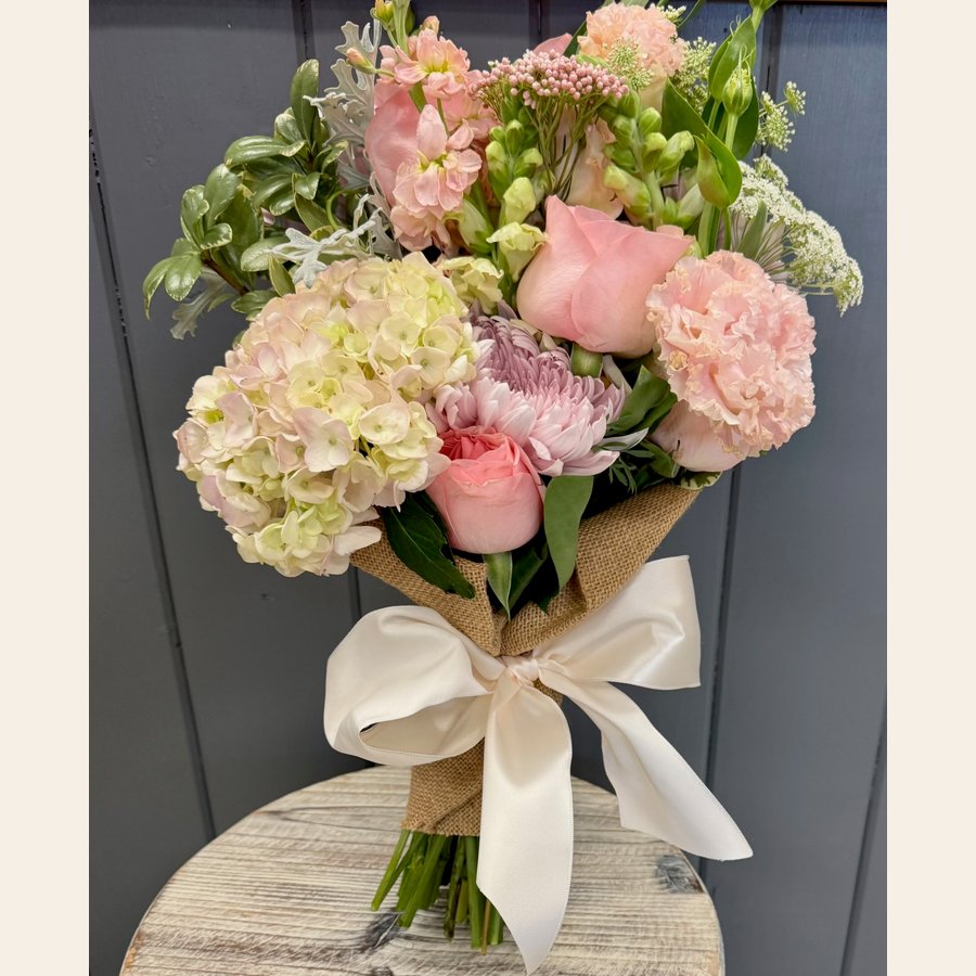 A pink rose and hydrangea handheld bouquet wrapped with burlap and a white bow